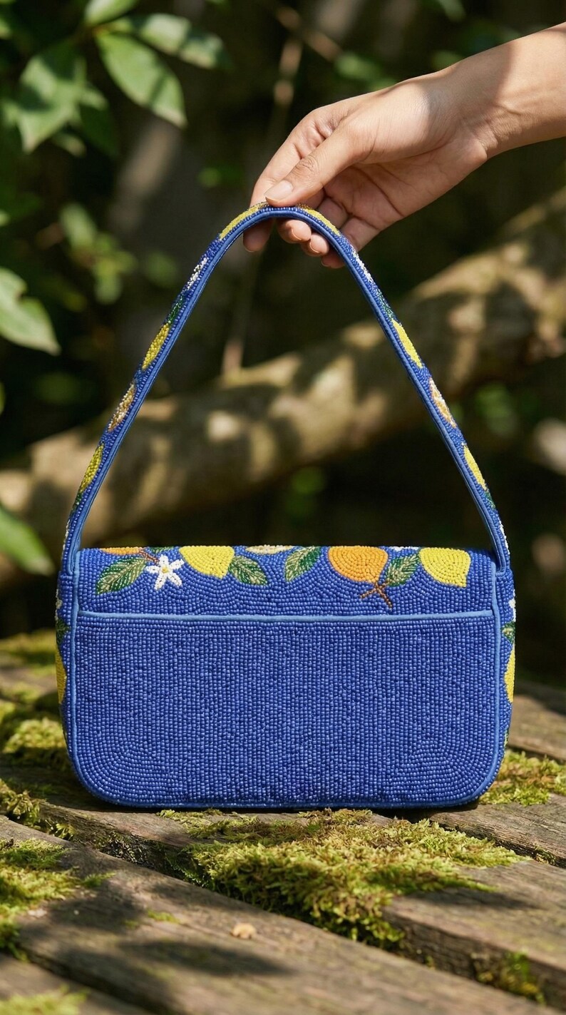 May include: A blue beaded handbag with a rectangular shape and a top handle. The bag is decorated with yellow lemons, white flowers, and green leaves. The handle and edges are also adorned with yellow and white beads.