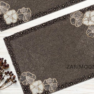 May include: Two brown beaded placemats with a white floral design and a black beaded border. The placemats have the text "ZariMoon" in the bottom right corner.