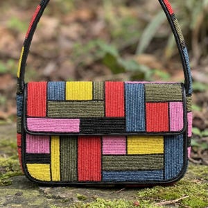 May include: A colorful beaded shoulder bag with a geometric pattern. The bag features a patchwork design with red, yellow, blue, pink, and green beads. It has a black leather trim and a matching strap.