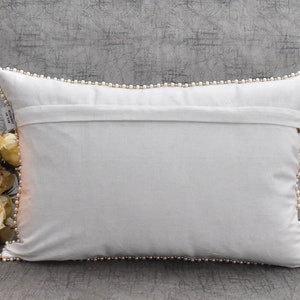 May include: White rectangular pillow with a white pearl trim around the edges. The pillow is lying flat on a gray textured surface.