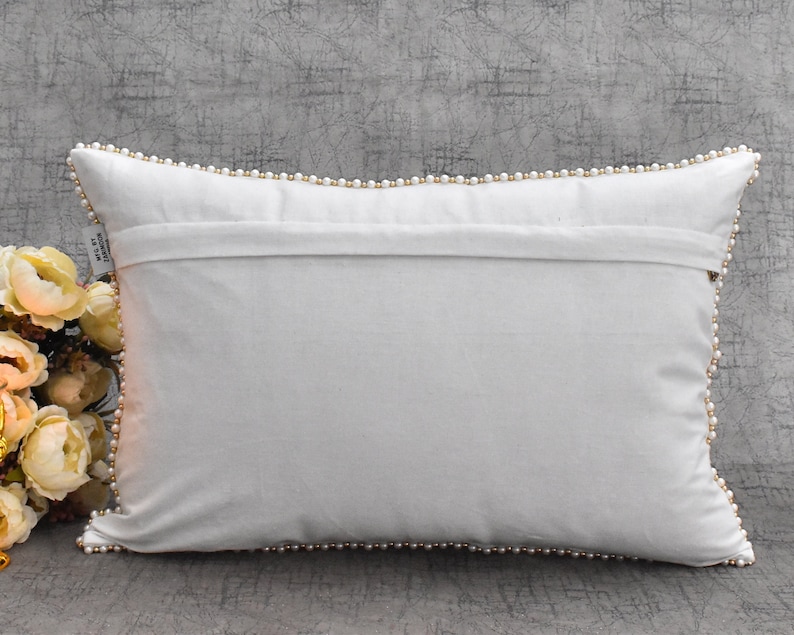 May include: White rectangular pillow with a white pearl trim around the edges. The pillow is lying flat on a gray textured surface.