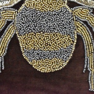 May include: A close-up of a beaded bumble bee with a gold and silver design. The bee is on a brown background.