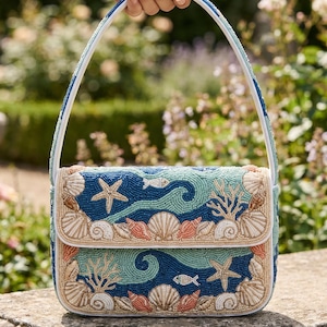 May include: A rectangular handbag featuring intricate beadwork in shades of blue, teal, and cream. The design displays an underwater scene with starfish, seashells, coral, and small fish. It includes a single beaded handle and a flap closure.
