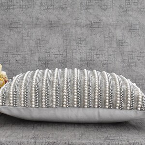 May include: A white pillow with a decorative design of silver and white beads arranged in horizontal rows.