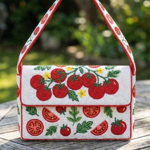 May include: A white beaded handbag with a red trim and handle. The bag is decorated with red tomatoes, green leaves, and yellow flowers. The tomatoes are in various sizes and arrangements, creating a vibrant and detailed design.