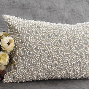 Puede incluir: Una funda de coj&iacute;n blanca con un patr&oacute;n decorativo de perlas blancas. Las perlas est&aacute;n dispuestas en un dise&ntilde;o de remolino en forma de onda.