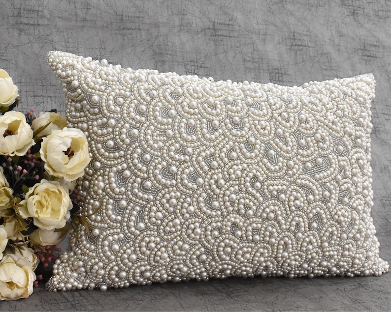 Puede incluir: Una funda de coj&iacute;n blanca con un patr&oacute;n decorativo de perlas blancas. Las perlas est&aacute;n dispuestas en un dise&ntilde;o de remolino en forma de onda.
