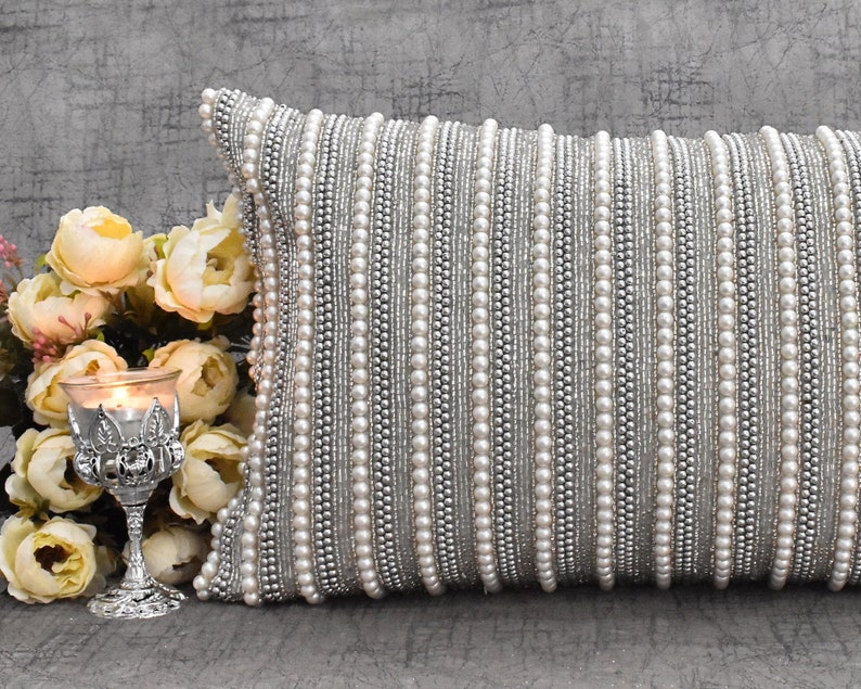 May include: A silver and white beaded throw pillow with a decorative design. The pillow is made of a soft fabric and has a luxurious feel.