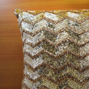 K&ouml;nnte beinhalten: Ein Kissen mit goldenen und silbernen Pailletten in einem Chevron-Muster.