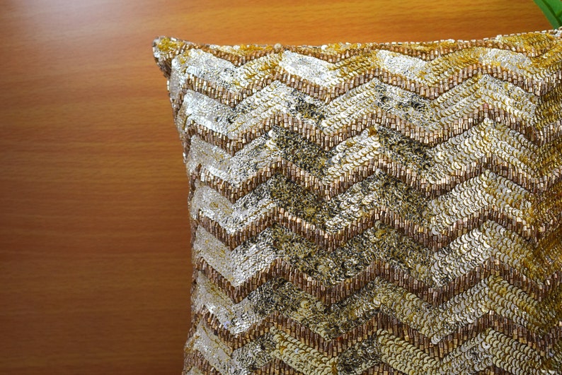 K&ouml;nnte beinhalten: Ein Kissen mit goldenen und silbernen Pailletten in einem Chevron-Muster.