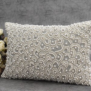 Puede incluir: Una almohada rectangular blanca con un patr&oacute;n decorativo de perlas blancas. La almohada est&aacute; hecha de una tela suave y tiene un brillo sutil. La almohada es perfecta para agregar un toque de elegancia a cualquier habitaci&oacute;n.