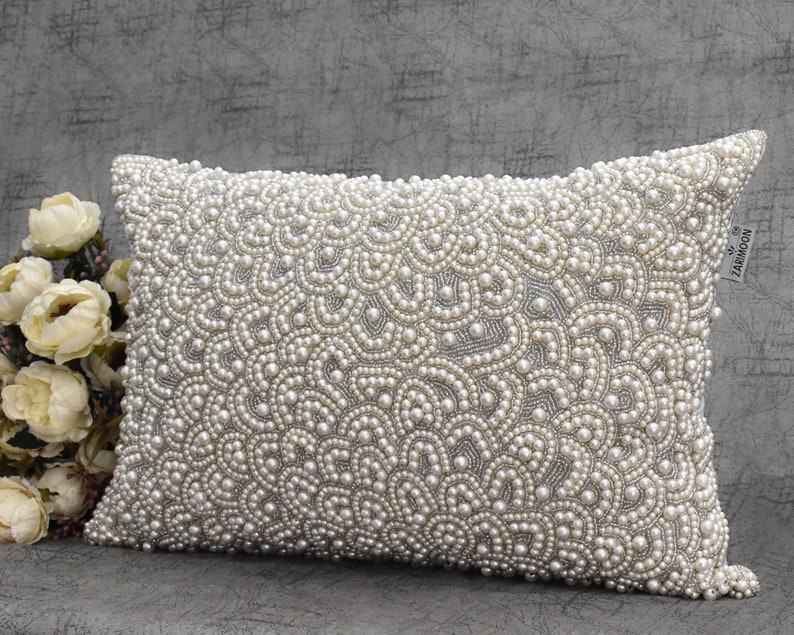Puede incluir: Una almohada rectangular blanca con un patr&oacute;n decorativo de perlas blancas. La almohada est&aacute; hecha de una tela suave y tiene un brillo sutil. La almohada es perfecta para agregar un toque de elegancia a cualquier habitaci&oacute;n.