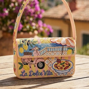 K&ouml;nnte beinhalten: Eine bestickte Handtasche mit gelbem Hintergrund und rosa Riemen. Die Tasche zeigt eine italienische Szene mit einem Roller, Zitronen und dem Schriftzug "La Dolce Vita". Das Design umfasst einen Sonnenschirm und einen Teller Pasta.