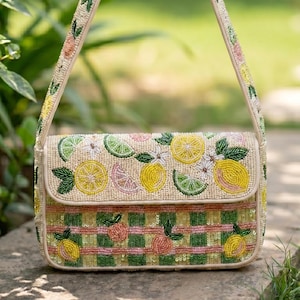 Puede incluir: Bolso de hombro bordado con temática de limones. El bolso presenta una base color crema con limones, limas y flores bordadas. La solapa tiene un diseño de limón, y la parte inferior tiene un patrón de cuadros verdes y rosas. La correa también está bordada.