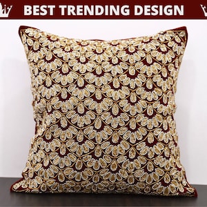 Pode incluir: Uma almofada de veludo vinho com um design de contas douradas e brancas. O design apresenta um padrão repetitivo de folhas e círculos.