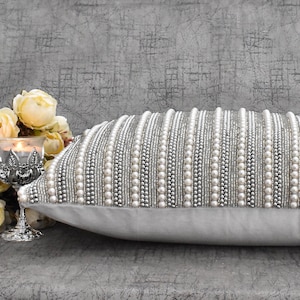May include: A white throw pillow with a silver and white beaded design. The pillow is made of a soft, luxurious fabric and is perfect for adding a touch of elegance to any room.