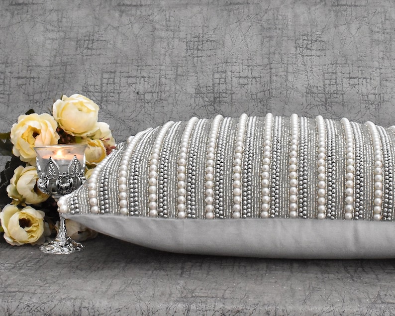 May include: A white throw pillow with a silver and white beaded design. The pillow is made of a soft, luxurious fabric and is perfect for adding a touch of elegance to any room.
