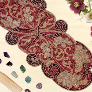 May include: A red and gold beaded table runner with a floral design. The runner is made of small beads and has a scalloped edge.