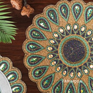 May include: A round beaded table mat with a peacock design. The mat is made of gold, green, and blue beads. The center of the mat has a smaller circle of beads in a darker shade of blue.