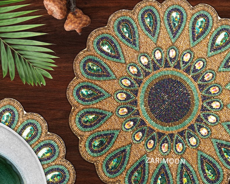 May include: A round beaded table mat with a peacock design. The mat is made of gold, green, and blue beads. The center of the mat has a smaller circle of beads in a darker shade of blue.