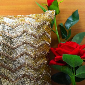 K&ouml;nnte beinhalten: Ein Kissen mit goldenen und silbernen Pailletten in einem Chevron-Muster, neben einer roten Rose mit gr&uuml;nen Bl&auml;ttern.