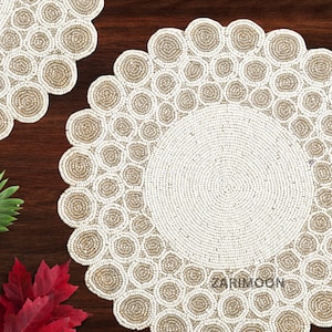 May include: Two white beaded placemats with a circular design. The placemats have a scalloped edge and are made of small white beads.