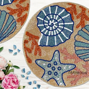 May include: Round beaded placemat with a beige background and a blue, white, and orange seashell design. The placemat features a starfish, coral, and seashells.