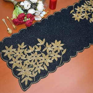 May include: Black beaded table runner with a gold floral design. The runner has a scalloped edge and is perfect for adding a touch of elegance to any table setting.