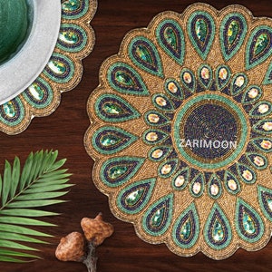 May include: A set of two round beaded placemats with a peacock feather design. The placemats are gold with green and blue accents. The placemats are made of beads and sequins.