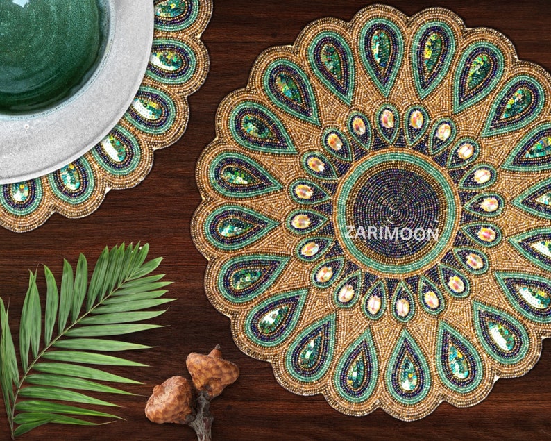 May include: A set of two round beaded placemats with a peacock feather design. The placemats are gold with green and blue accents. The placemats are made of beads and sequins.
