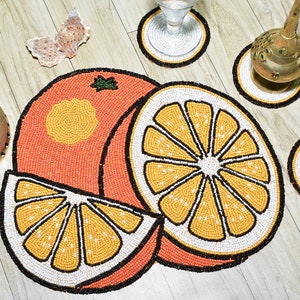 May include: Set of four orange slice beaded coasters. The coasters are round and feature a detailed design of orange slices with yellow and white beads. The coasters are perfect for adding a touch of whimsy to your home decor.