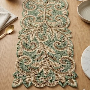Könnte beinhalten: Ein Tischläufer aus Perlen in Grün-, Beige- und Goldtönen. Der Läufer hat ein aufwendiges Blumen- und Scroll-Design. Die Kanten sind gewellt, was dem Esstisch eine dekorative Note verleiht.