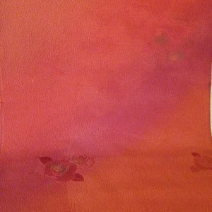 May include: A close-up of a textured, red fabric with a gradient of pink hues. Faint floral patterns are visible, adding a subtle decorative element to the textile. The fabric's surface appears slightly uneven.