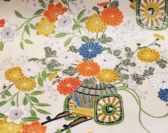 May include: A white fabric with a floral pattern featuring orange, yellow, blue, and green flowers. Two small, ornate, blue and gold carriages are on a black track with wheels.