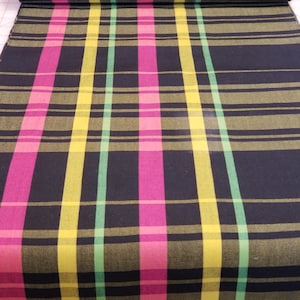 May include: A roll of fabric with a plaid pattern. The fabric features a dark navy blue background with vertical and horizontal stripes in pink, yellow, and light green. The fabric is rolled up at the top, showing the pattern.