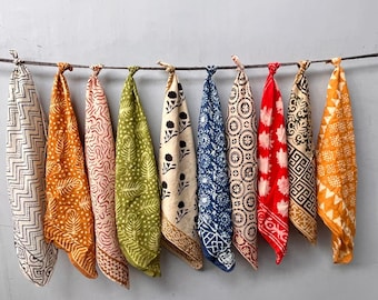 May include: A collection of ten colorful, patterned bandanas hanging from a wire. The bandanas display various designs, including geometric shapes, floral patterns, and abstract motifs. Colors include white, orange, red, green, and blue, creating a vibrant display.