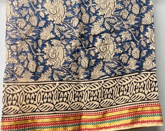 May include: A blue and cream floral patterned textile. The fabric displays a large floral design with a border of repeating patterns. The bottom edge has a stripe of red, yellow, and green. The textile is likely cotton or a similar fabric.