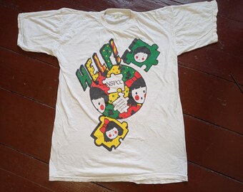 May include: White t-shirt with a colorful graphic design featuring the word "HELP!" and cartoon children's faces. The graphic also includes the text "NSPCC" and "National Society for the Prevention of Cruelty to Children Appeal."