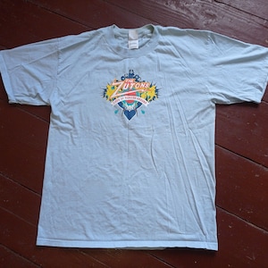 Op de afbeelding: Lichtblauw T-shirt met een kleurrijke afbeelding van "The Zutons" en de tekst "Years of Hanging Around".