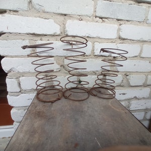 May include: Three rusty metal springs stacked on top of each other on a wooden surface. The springs are coiled and have a diameter of about 6 inches.