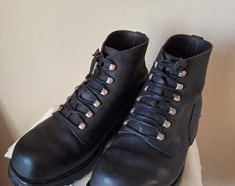 Op de afbeelding: Een paar zwarte leren enkellaarzen met een ronde neus, een dikke rubberen profielzool en zilverkleurige metalen D-ring veterogen. De laarzen hebben een hoog model met een treklipje aan de achterkant van de schacht.
