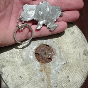 May include: A silver metal keychain shaped like the outline of Kazakhstan. The keychain is attached to a silver chain and ring.