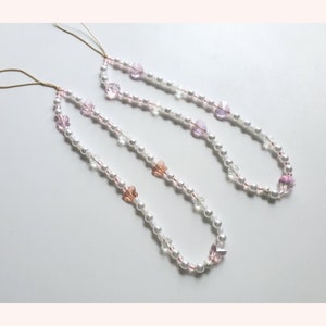 May include: Two white pearl necklaces with pink and clear crystal beads and pink butterfly charms.