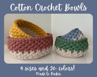 May include: Three cotton crochet bowls in different sizes and colors. The largest bowl is a two-tone design with a light pink and white base and a yellow top. The medium bowl is a solid light pink. The smallest bowl is a two-tone design with a white base and a green top. The bowls are on a white surface. 4 sizes and 20+ colors! Made to order.