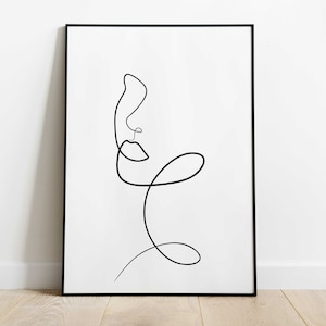 May include: A black framed print featuring a minimalist line drawing of a face. The drawing is in black ink on a white background.