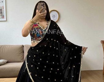 May include: A black velvet sari with white dot accents and a gold trim. The sari is paired with a colorful embroidered top and a matching black skirt. The text "VANDANFAB" is visible on the top.