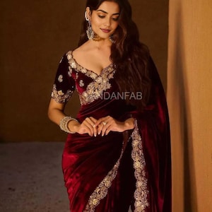 May include: A deep burgundy velvet saree with elaborate gold embroidery on the edges and bodice. The saree has a low V-neck and short sleeves with gold embellishments. The text "ANDANFAB" is visible on the garment.