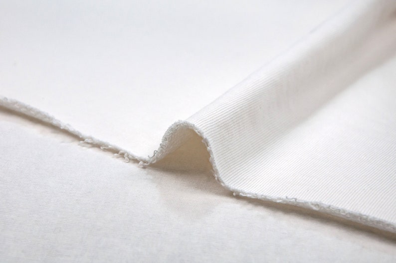 May include: Close-up of a white ribbed fabric folded over itself. The fabric is soft and has a slightly textured surface.