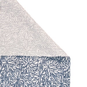 May include: A white fabric with a textured pattern, folded over to reveal a blue fabric with a floral pattern.