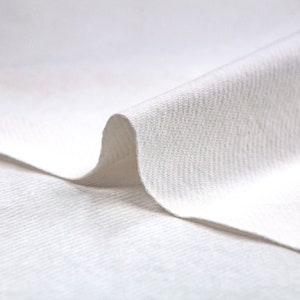 May include: Close-up of a white fabric with a textured surface. The fabric is folded over itself, creating a soft, curved shape.